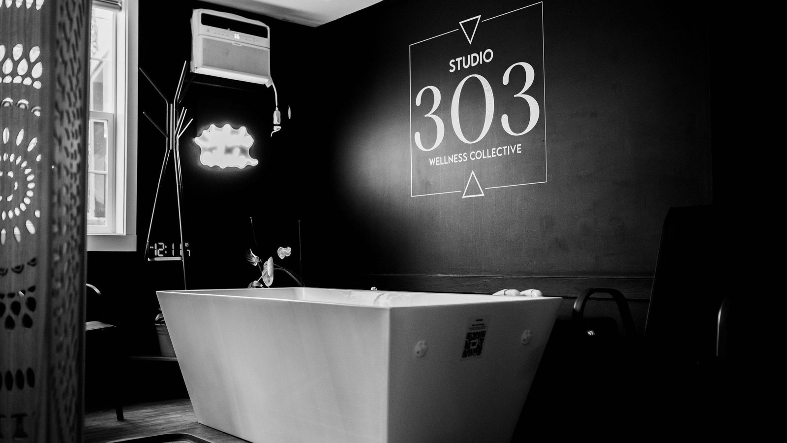 The cold plunge tub lit by the Studio 303 sign in the private session room